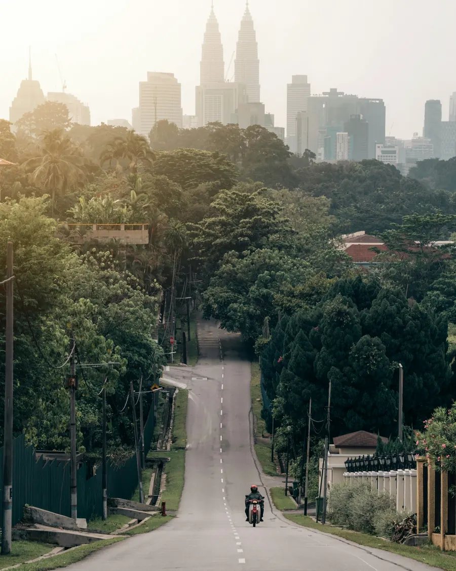 Jalan sunyi berpokok di Bangsar, dengan menara bandar kelihatan di sebalik jerebu