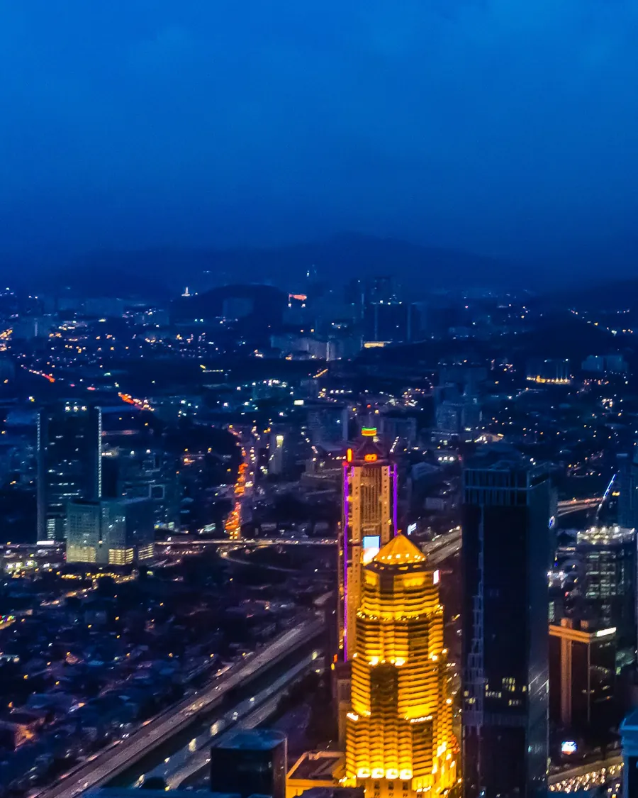 Pusat Kuala Lumpur waktu senja, dengan menara bercahaya keemasan dan aliran trafik
